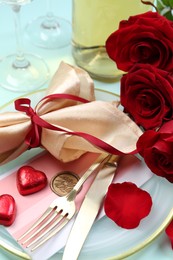 Photo of Romantic place setting with cutlery, hearts and red roses on light blue background, closeup. Valentine's day celebration