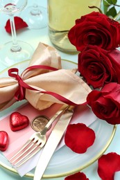 Photo of Romantic place setting with cutlery, hearts and red roses on light blue background, closeup. Valentine's day celebration