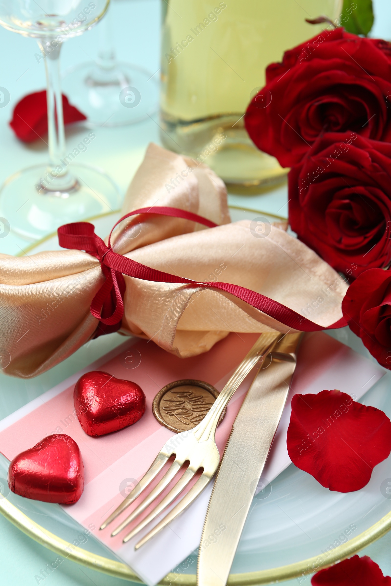 Photo of Romantic place setting with cutlery, hearts and red roses on light blue background, closeup. Valentine's day celebration