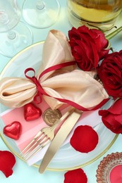 Photo of Romantic place setting with cutlery, hearts and red roses on light blue background, flat lay. Valentine's day celebration