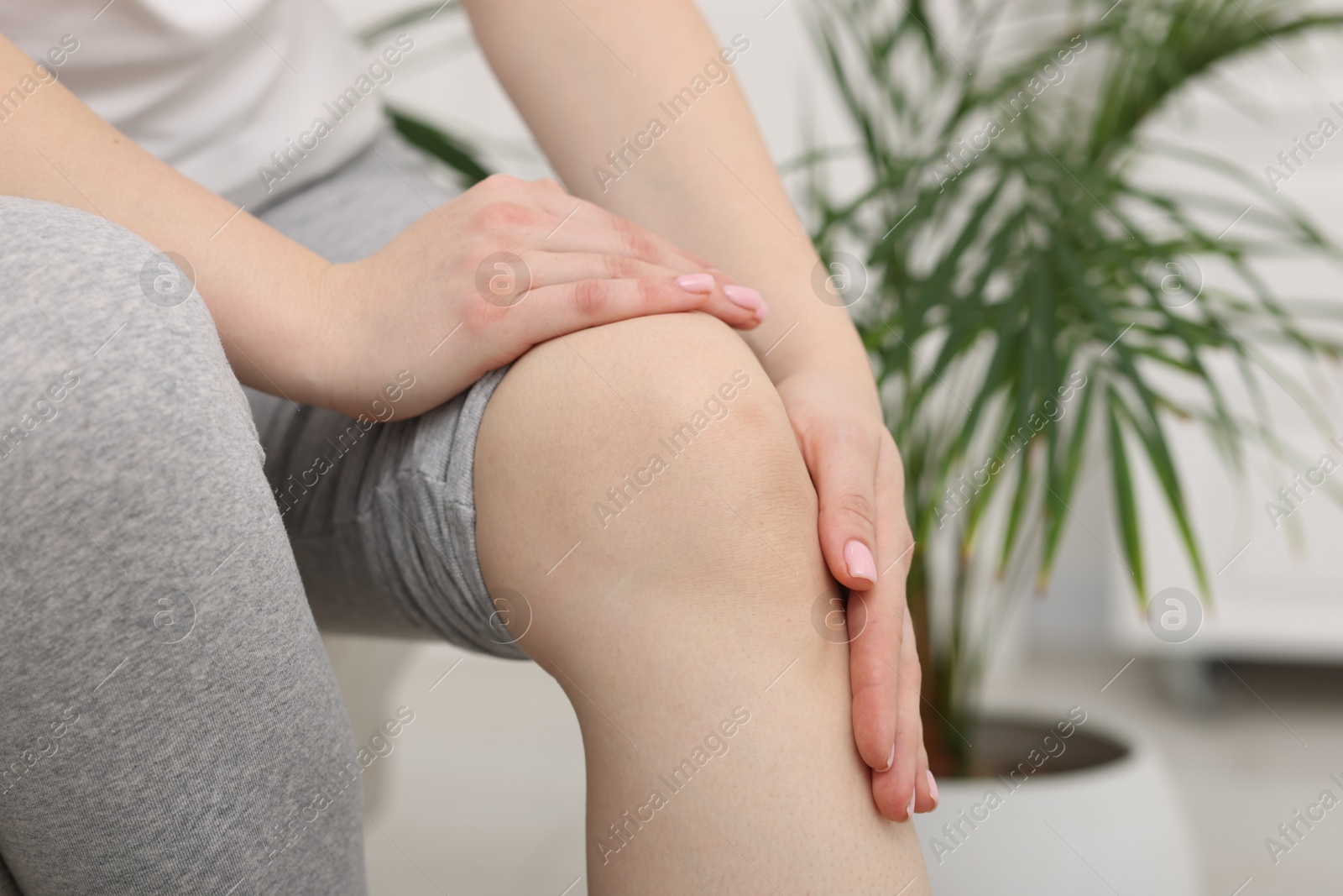 Photo of Young woman suffering from pain in knee at home, closeup