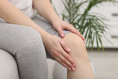 Photo of Young woman suffering from pain in knee on sofa at home, closeup