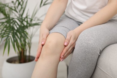 Photo of Young woman suffering from pain in knee on sofa at home, closeup