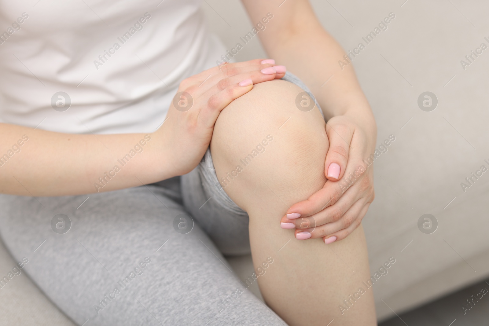 Photo of Young woman suffering from pain in knee on sofa at home, closeup