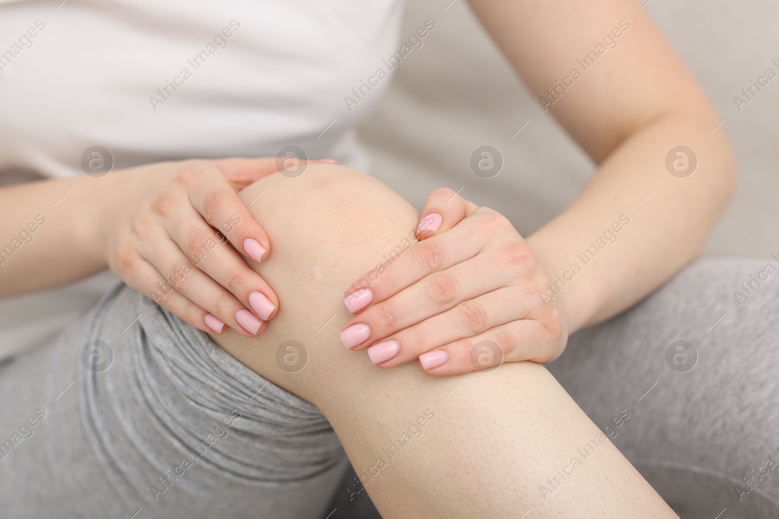 Photo of Young woman suffering from pain in knee on sofa at home, closeup