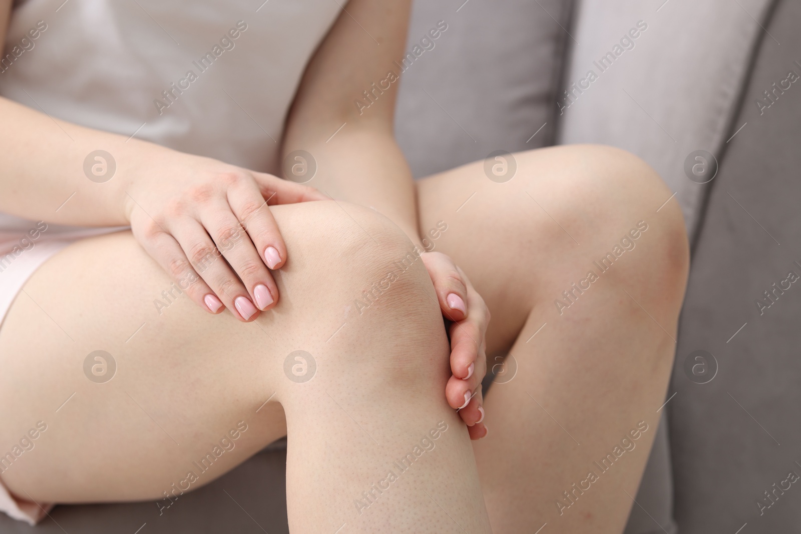 Photo of Young woman suffering from pain in knee on sofa at home, closeup