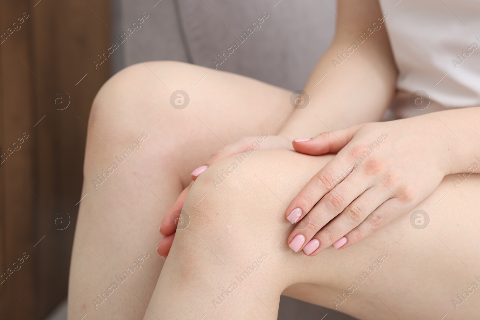 Photo of Young woman suffering from pain in knee at home, closeup