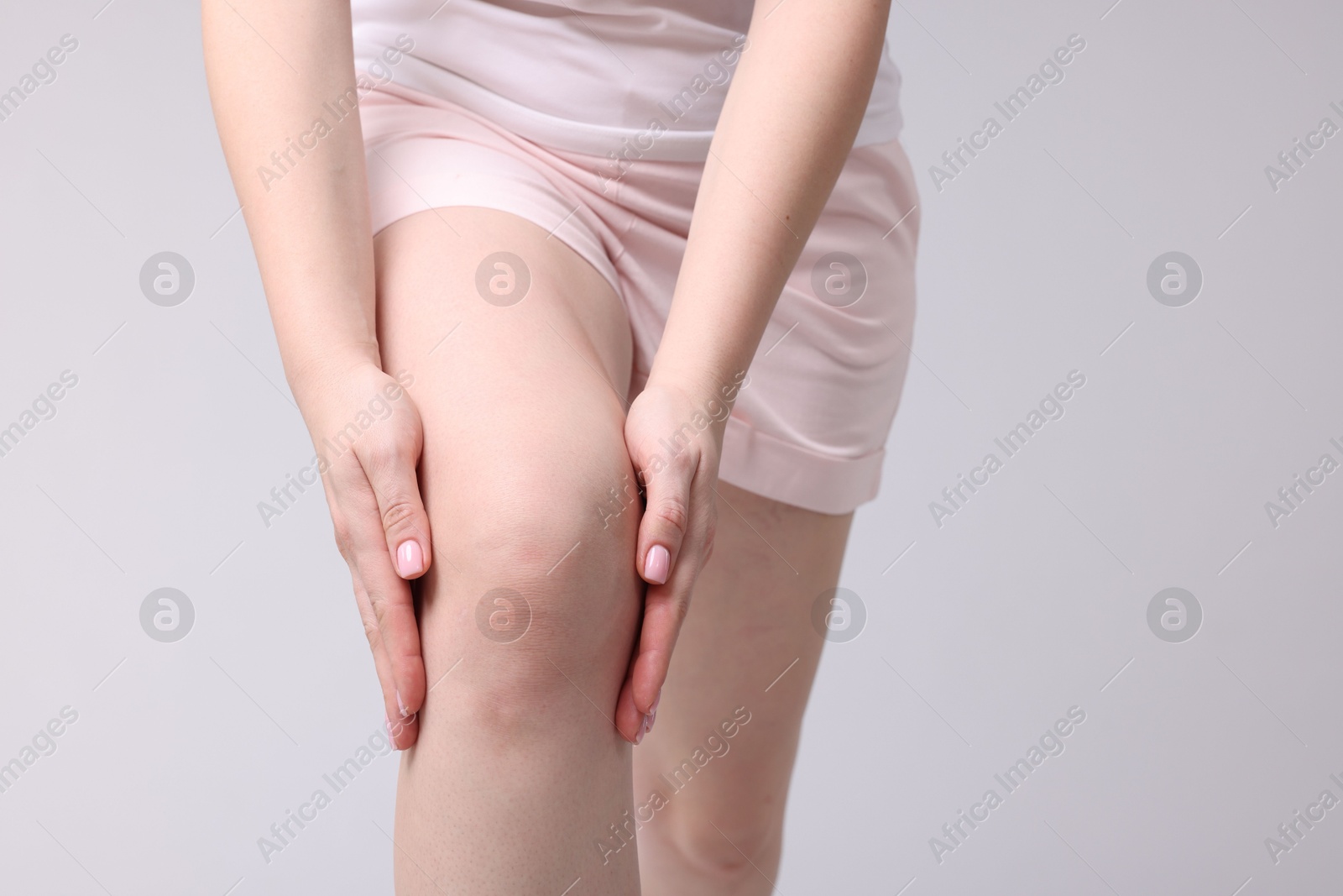 Photo of Young woman suffering from pain in knee on light grey background, closeup