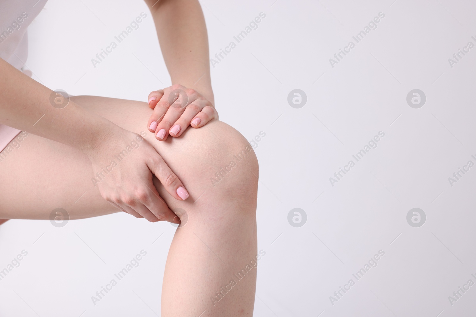 Photo of Young woman suffering from pain in knee on light grey background, closeup. Space for text