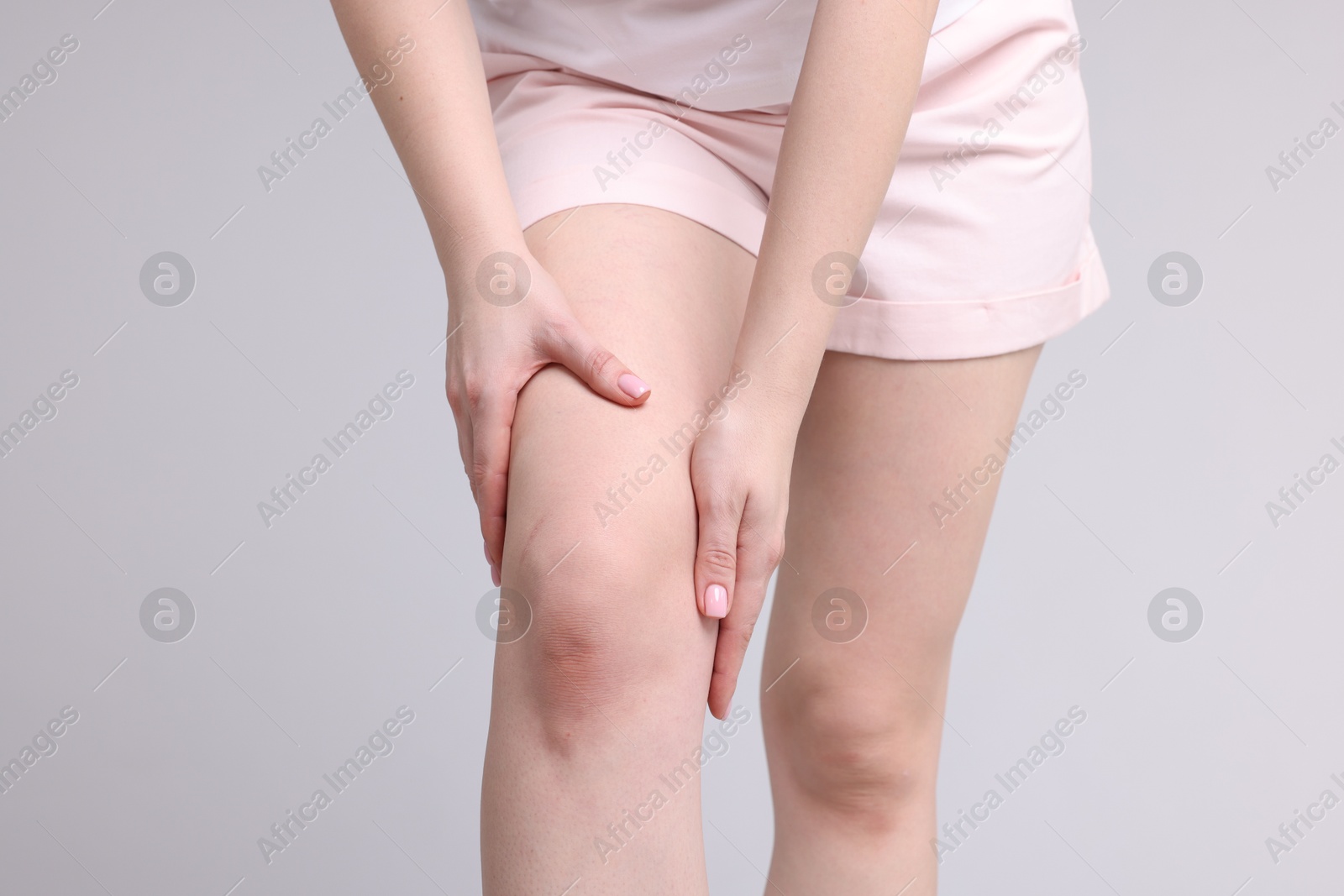 Photo of Young woman suffering from pain in knee on light grey background, closeup