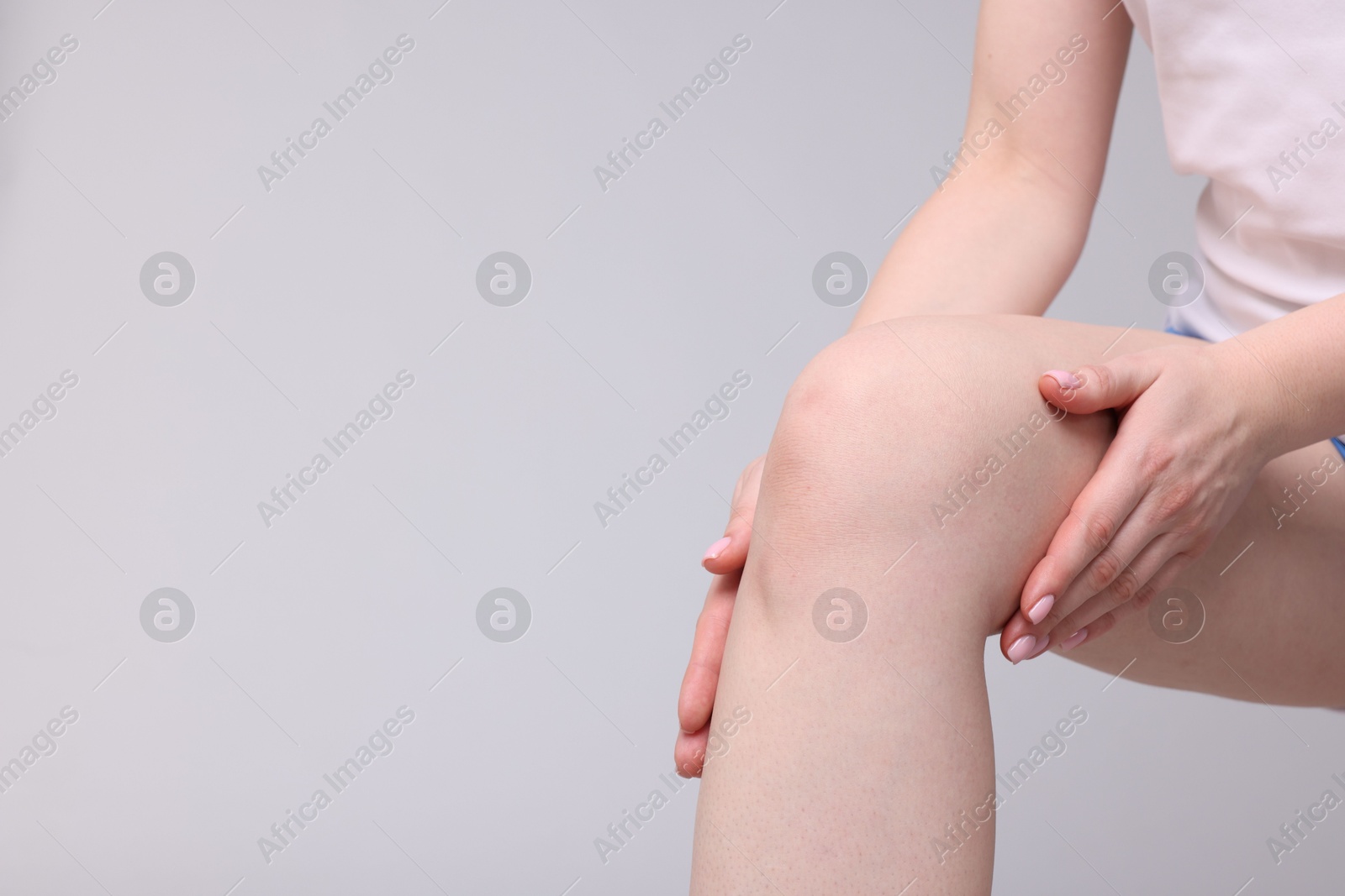 Photo of Young woman suffering from pain in knee on light grey background, closeup. Space for text