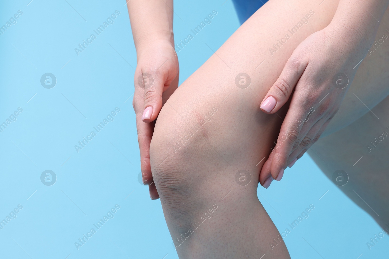 Photo of Young woman suffering from pain in knee on light blue background, closeup