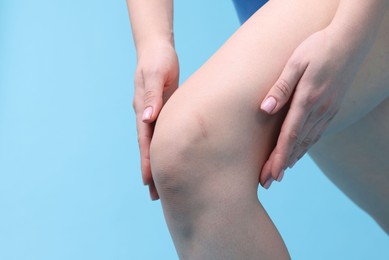 Photo of Young woman suffering from pain in knee on light blue background, closeup