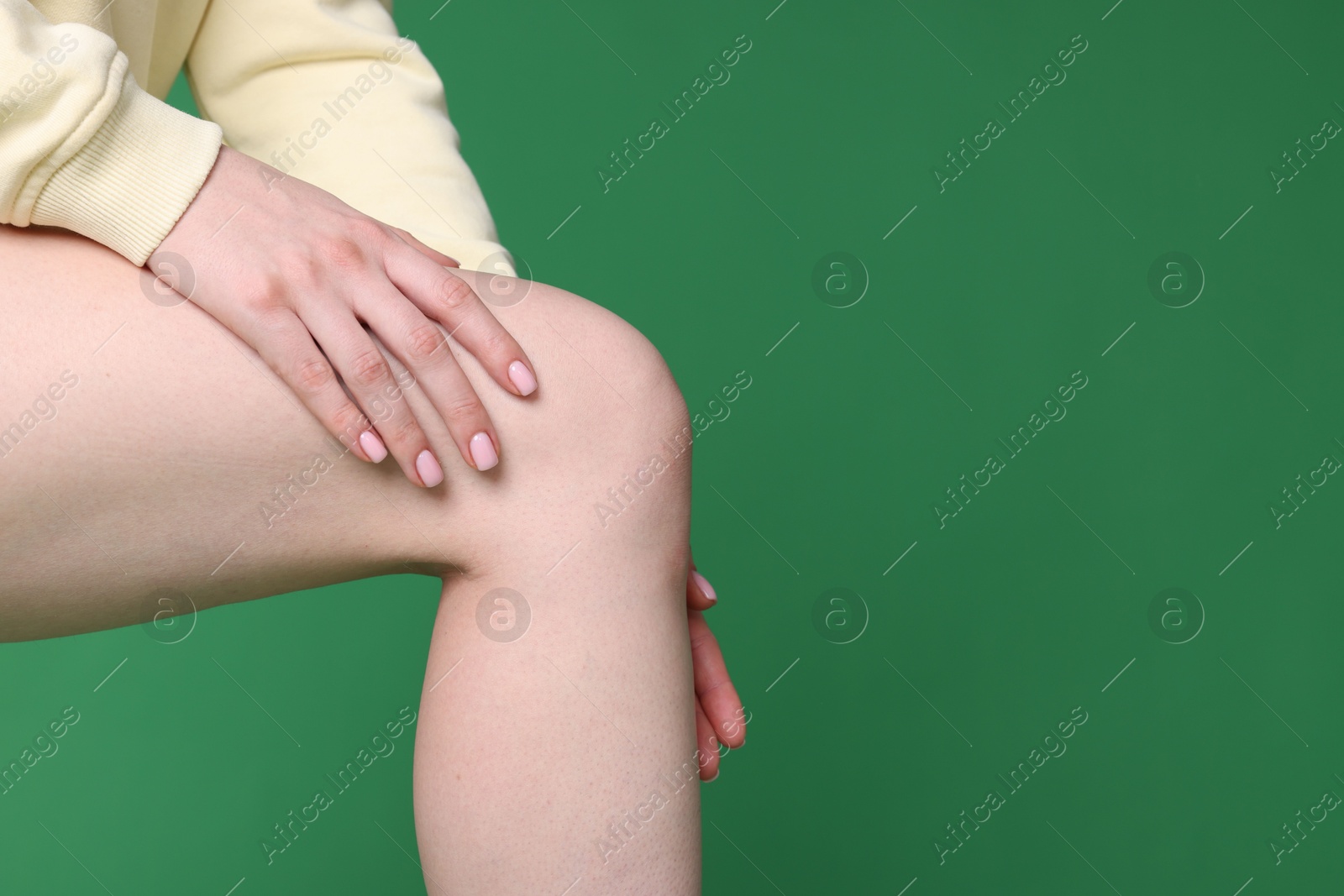 Photo of Young woman suffering from pain in knee on green background, closeup. Space for text