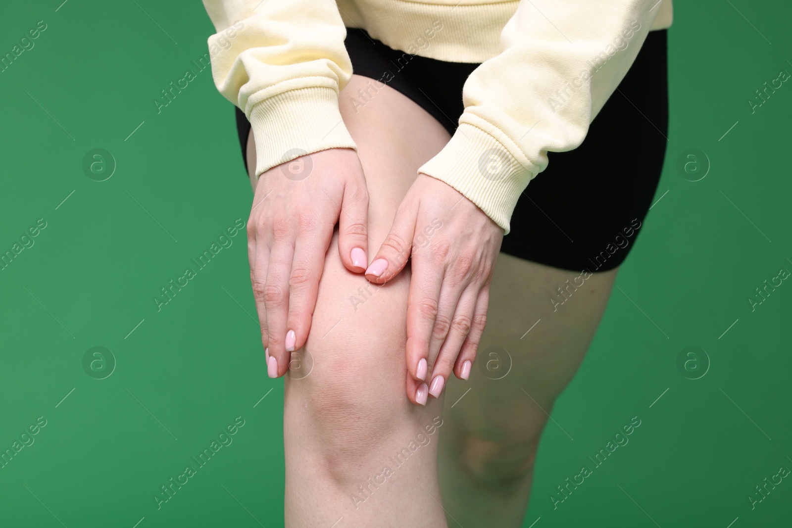 Photo of Young woman suffering from pain in knee on green background, closeup