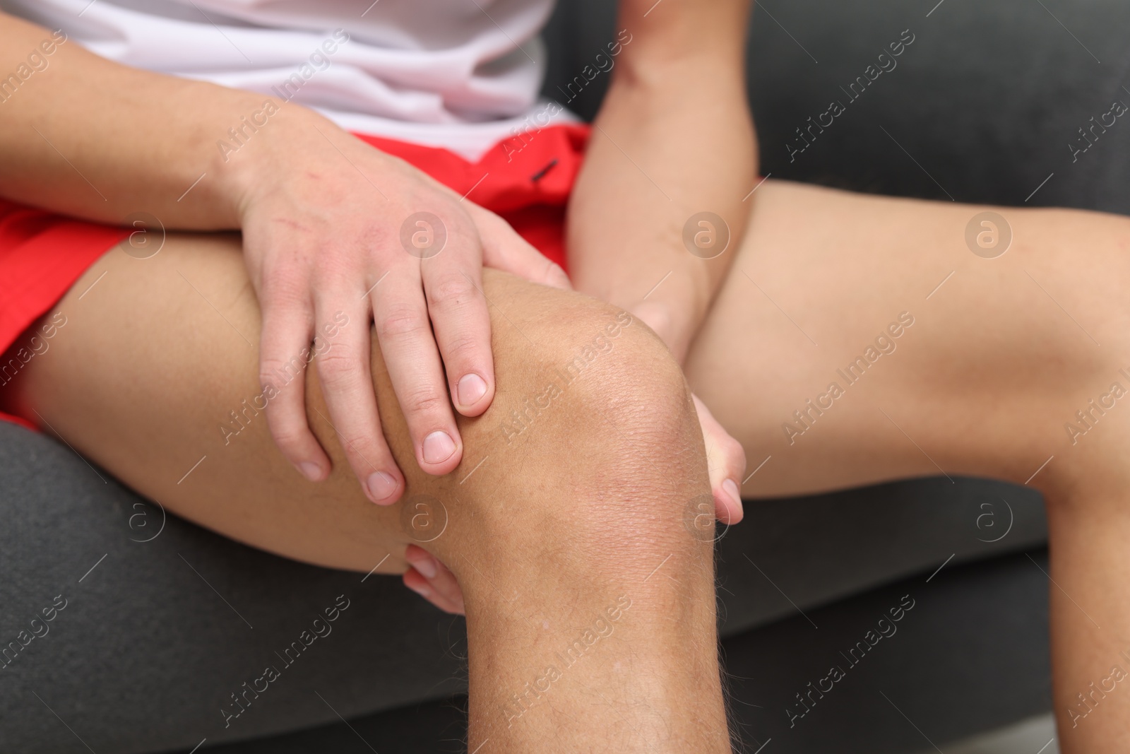 Photo of Young man suffering from pain in knee on sofa at home, closeup