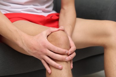 Photo of Young man suffering from pain in knee on sofa at home, closeup