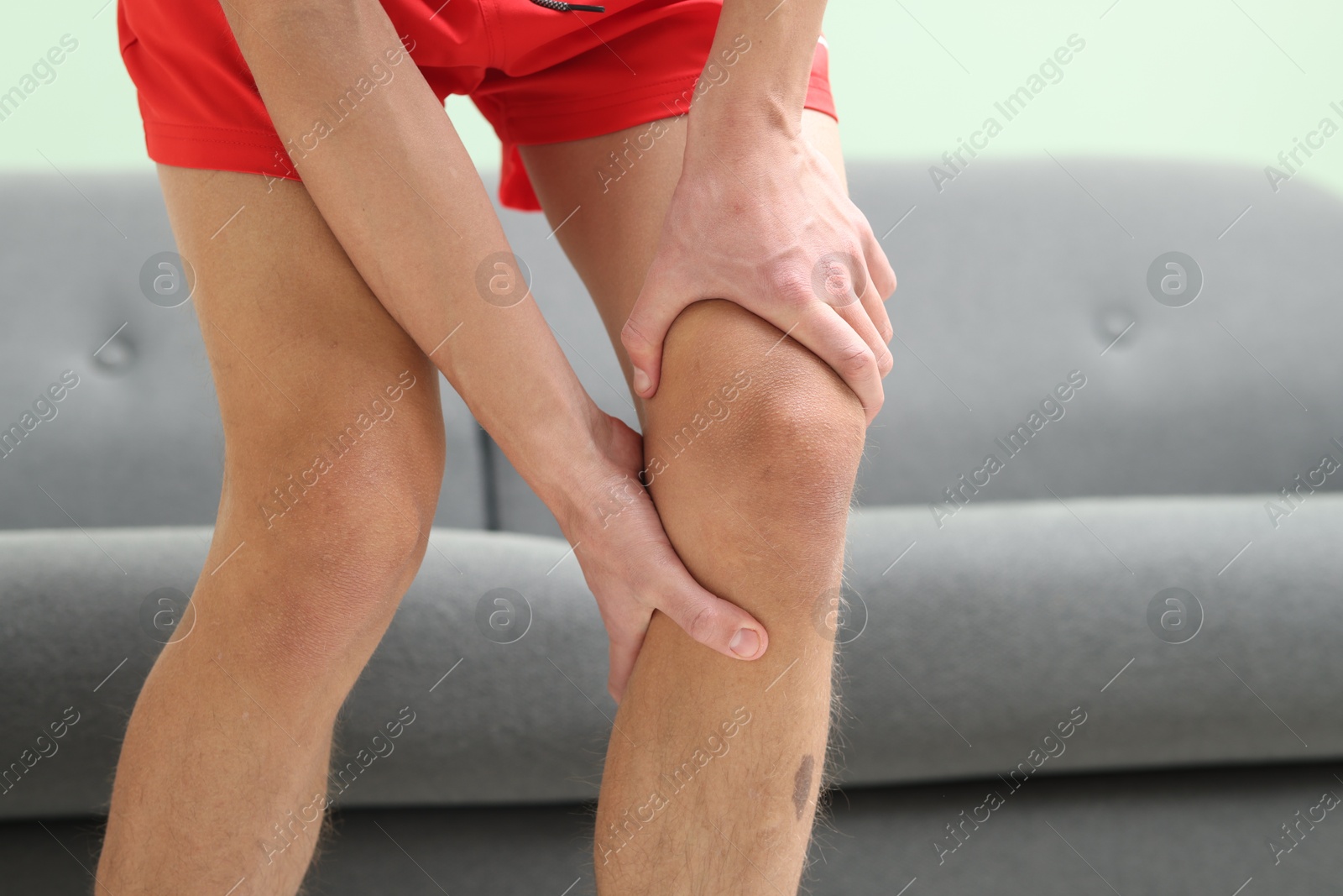 Photo of Young man suffering from pain in knee at home, closeup