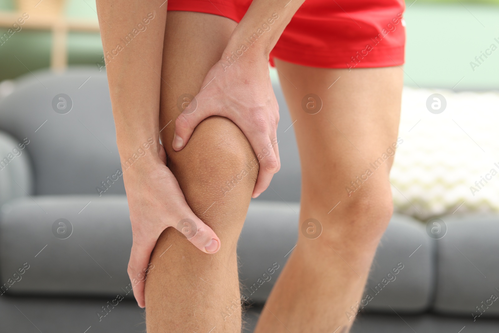 Photo of Young man suffering from pain in knee at home, closeup