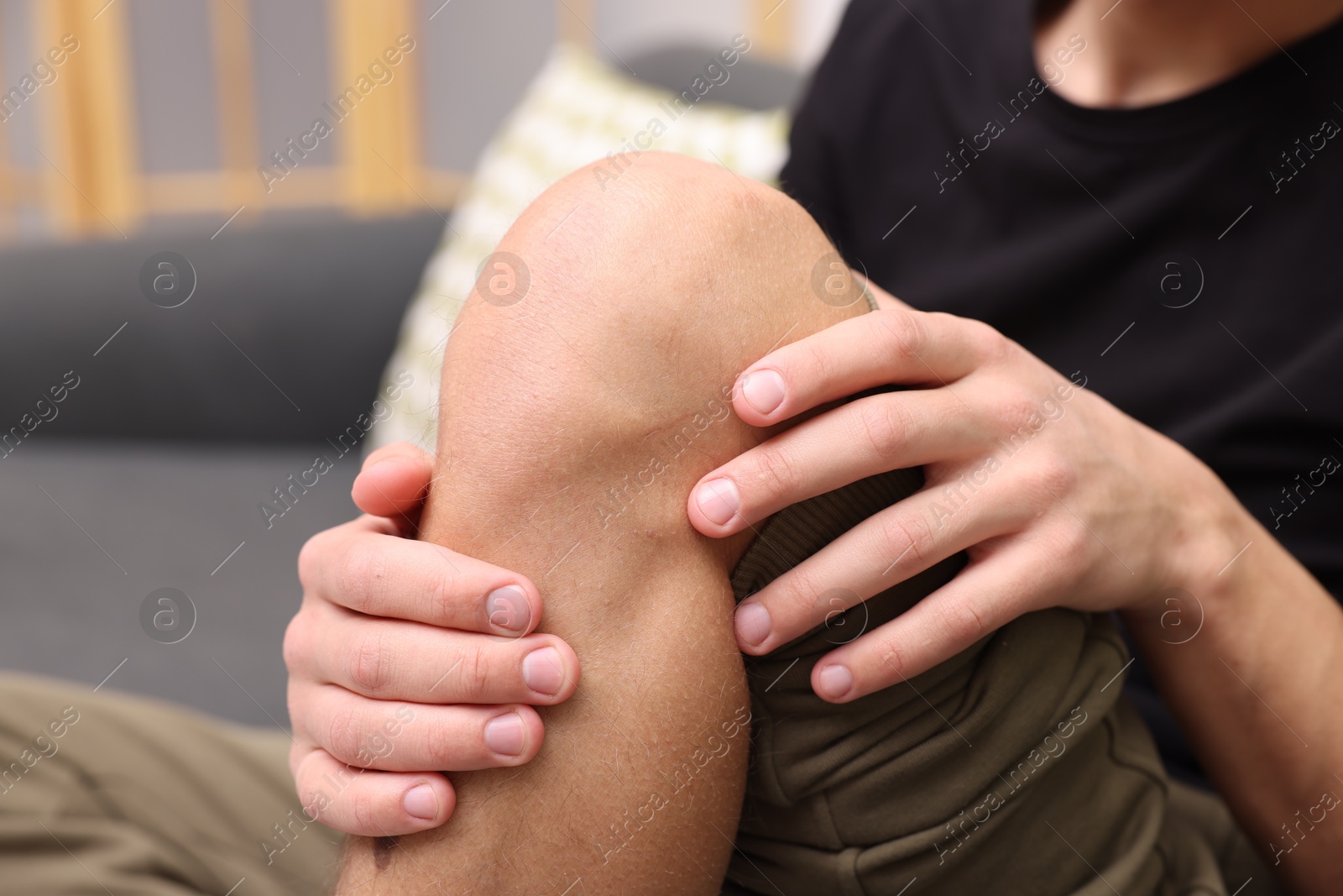 Photo of Young man suffering from pain in knee on sofa at home, closeup