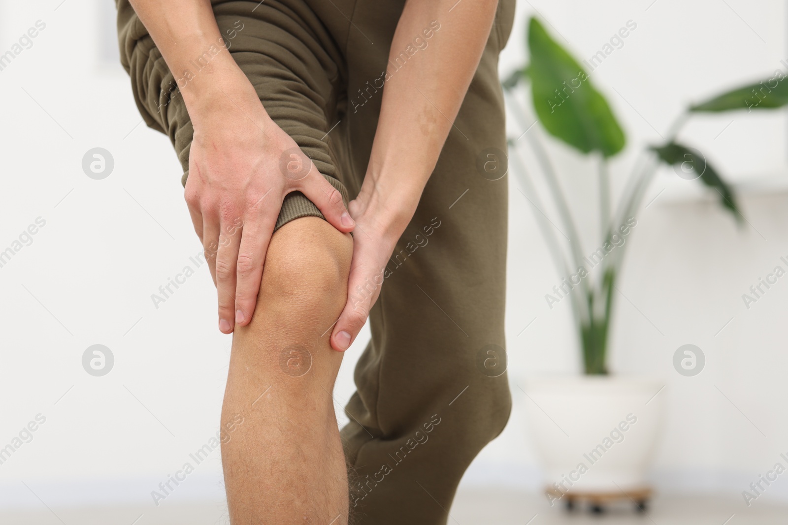 Photo of Young man suffering from pain in knee at home, closeup