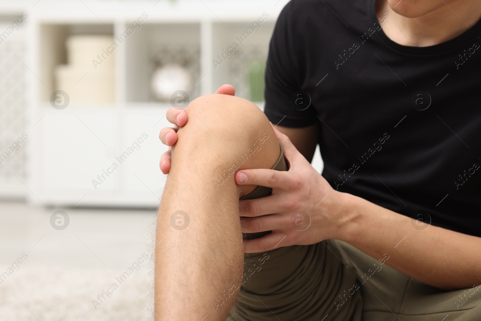 Photo of Young man suffering from pain in knee at home, closeup. Space for text