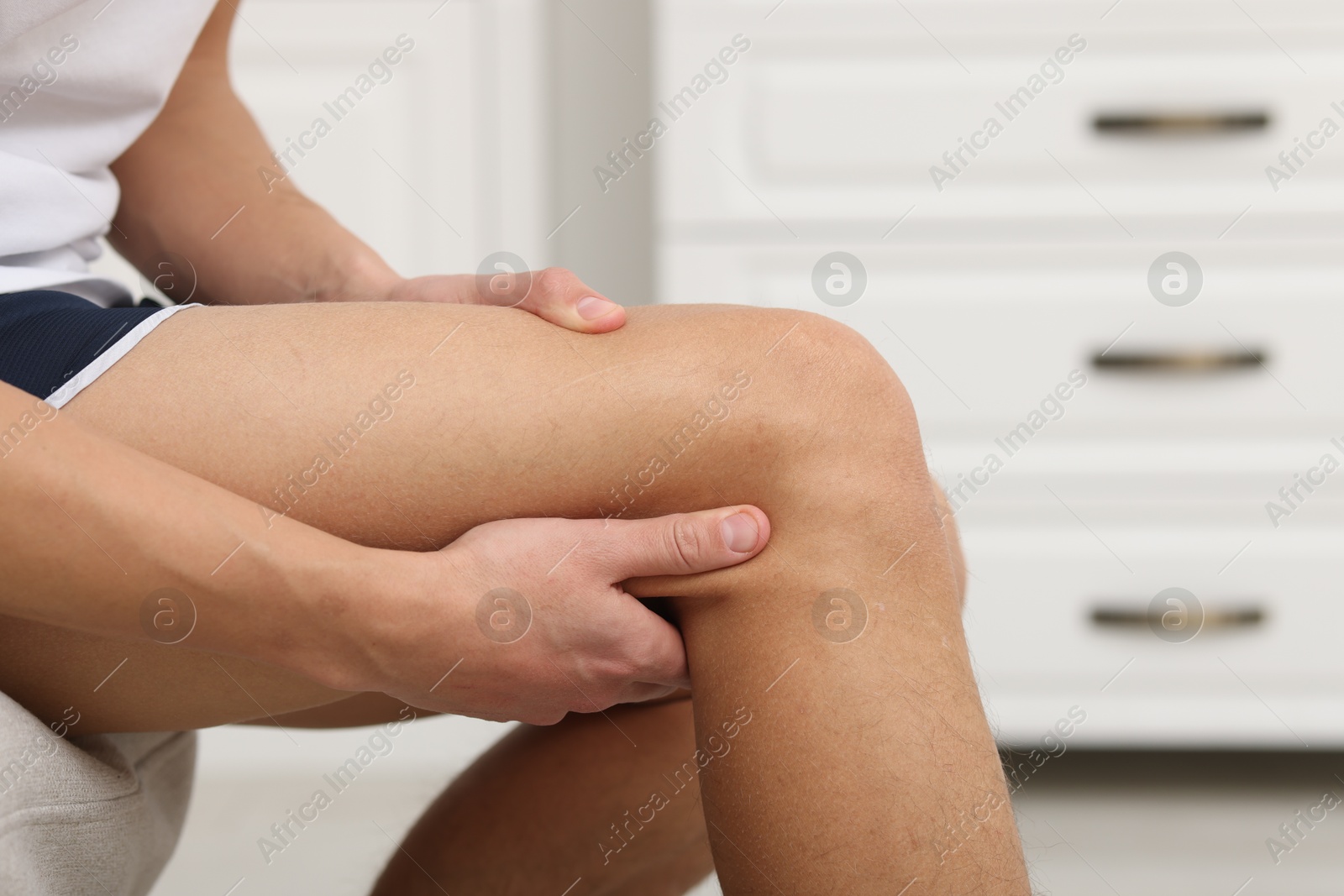 Photo of Young man suffering from pain in knee on sofa at home, closeup