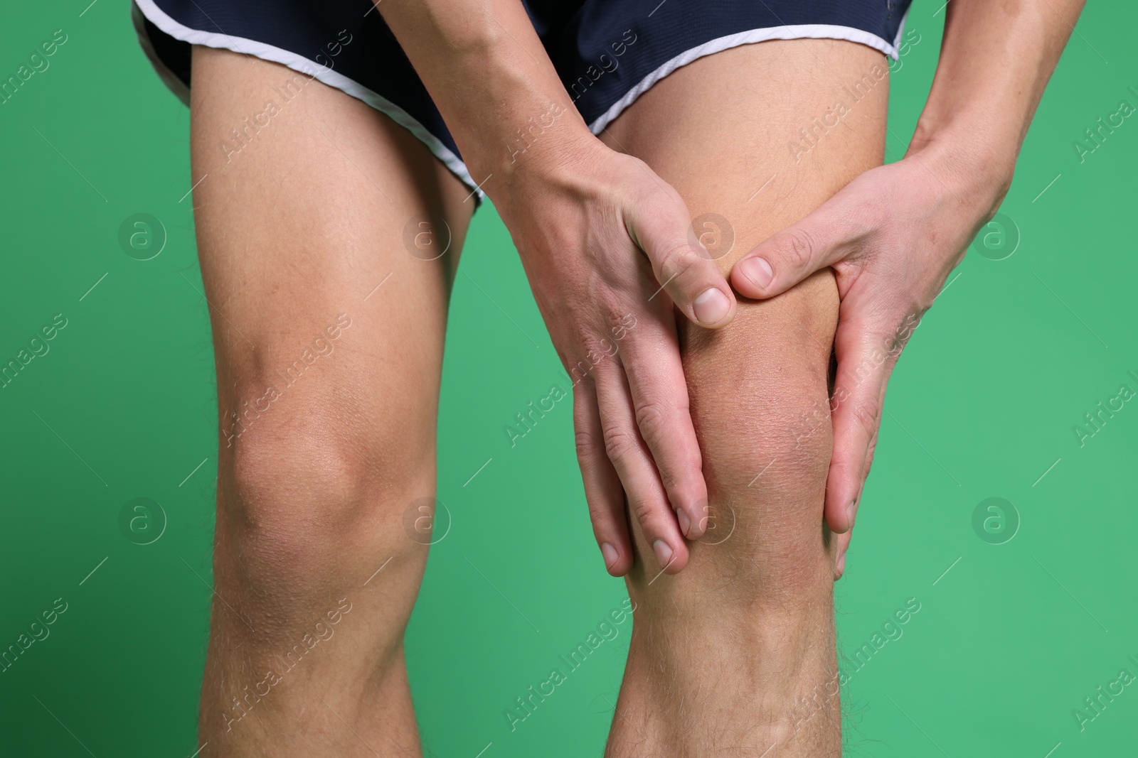 Photo of Young man suffering from pain in knee on green background, closeup