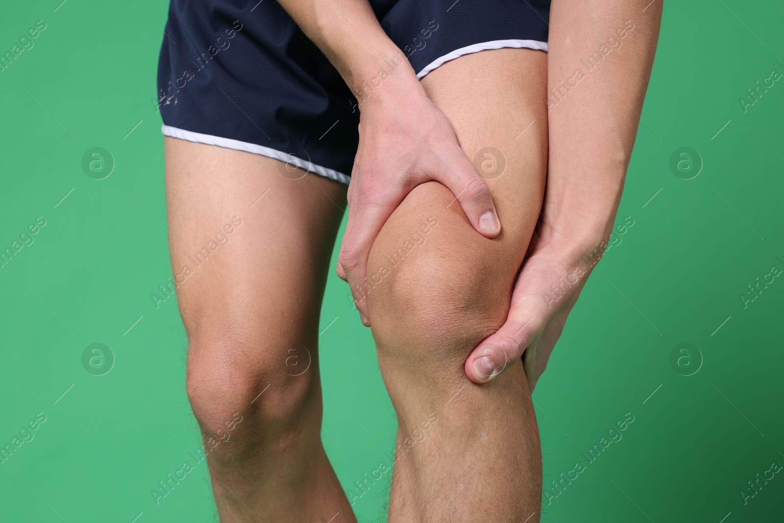 Photo of Young man suffering from pain in knee on green background, closeup