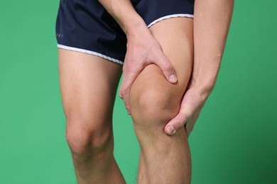 Photo of Young man suffering from pain in knee on green background, closeup