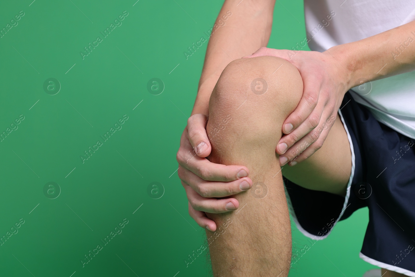 Photo of Young man suffering from pain in knee on green background, closeup. Space for text