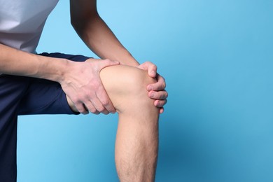 Photo of Young man suffering from pain in knee on light blue background, closeup. Space for text