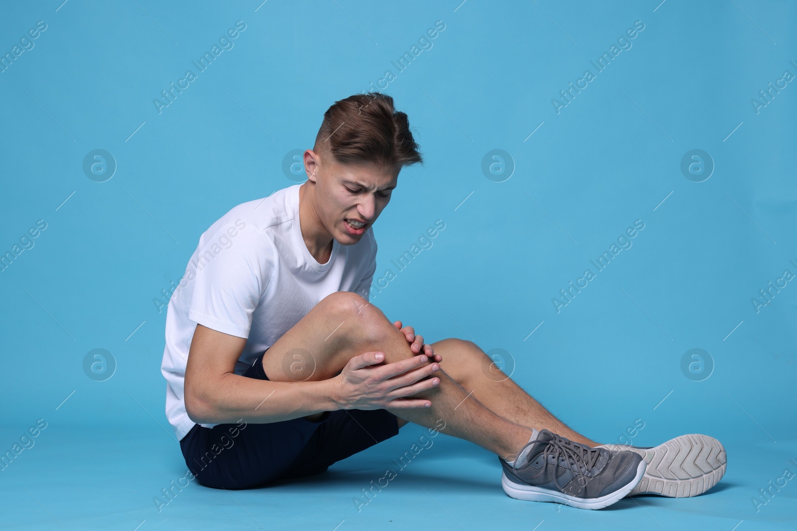 Photo of Young man suffering from pain in knee on light blue background