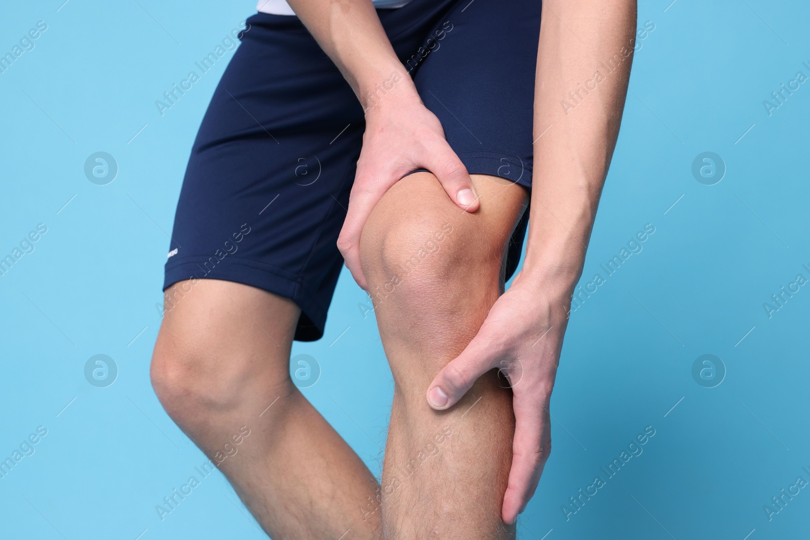 Photo of Young man suffering from pain in knee on light blue background, closeup