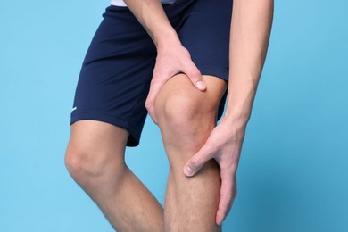 Photo of Young man suffering from pain in knee on light blue background, closeup