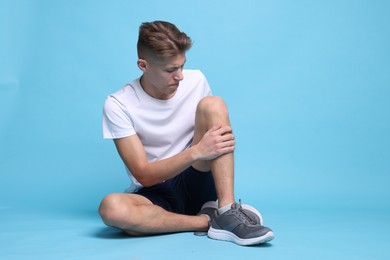 Photo of Young man suffering from pain in knee on light blue background