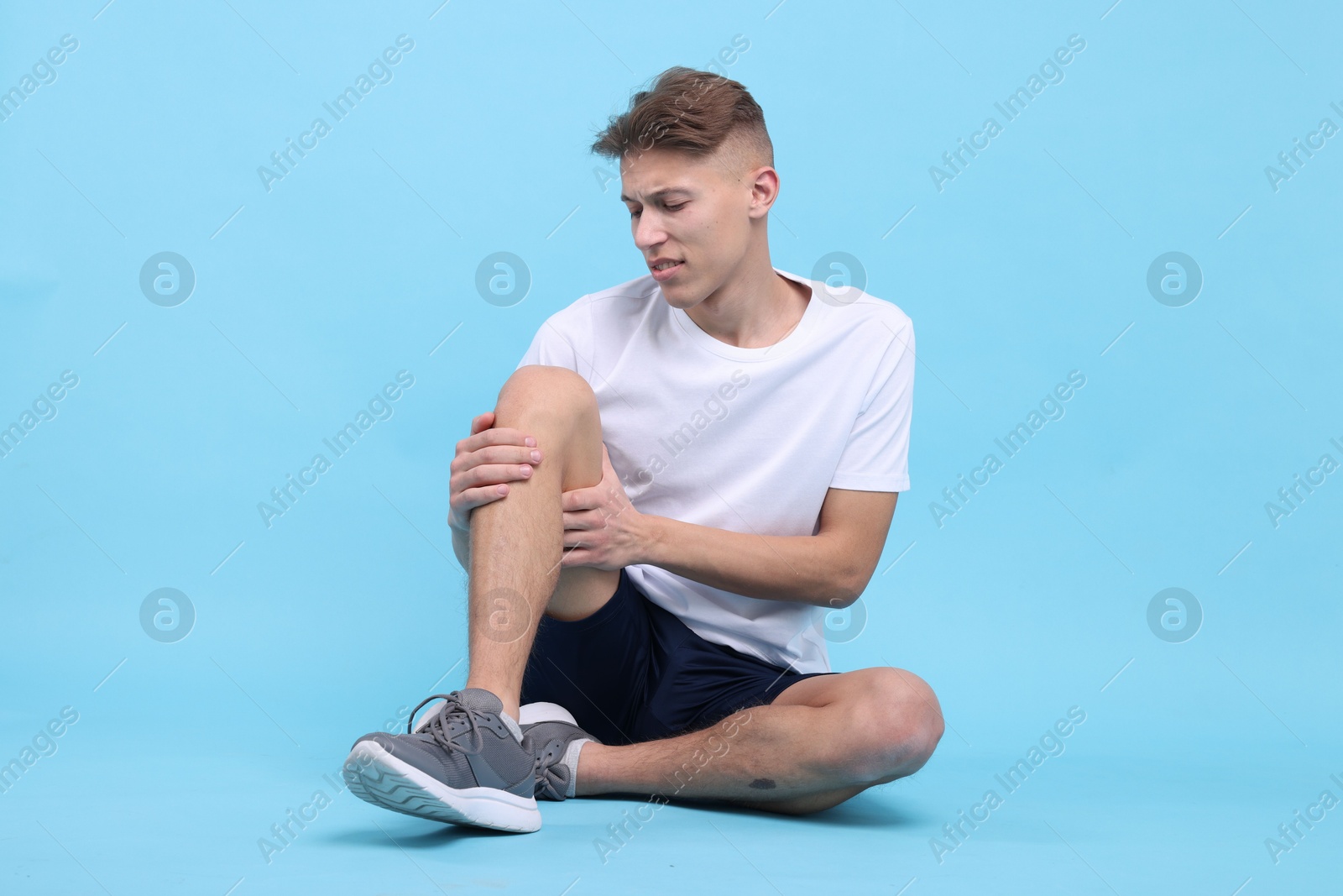 Photo of Young man suffering from pain in knee on light blue background