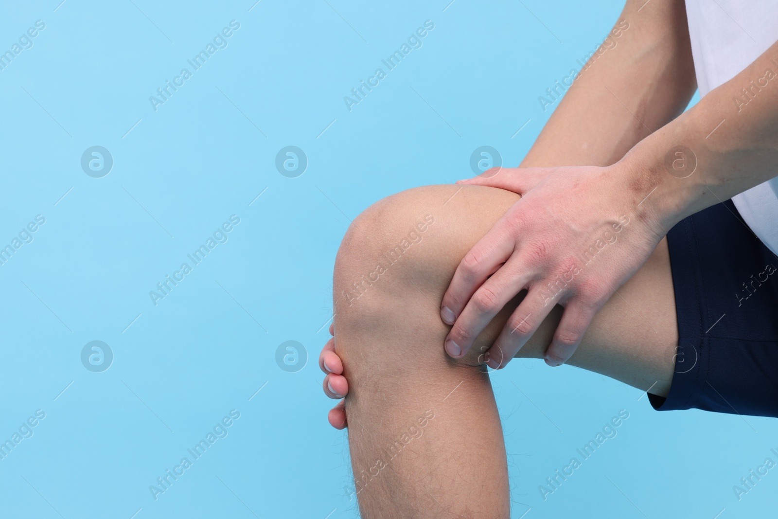 Photo of Young man suffering from pain in knee on light blue background, closeup. Space for text