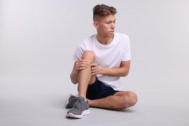 Photo of Young man suffering from pain in knee on light grey background