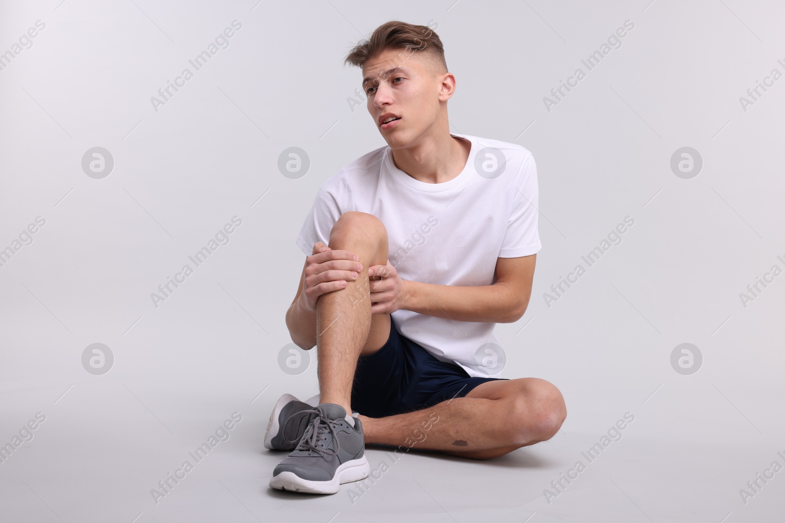 Photo of Young man suffering from pain in knee on light grey background