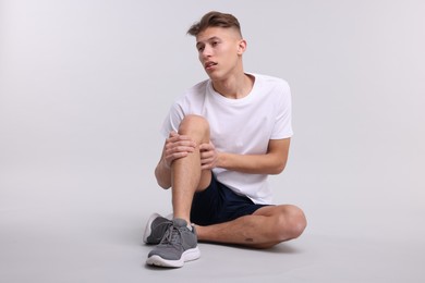 Photo of Young man suffering from pain in knee on light grey background