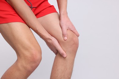 Photo of Young man suffering from pain in knee on light grey background, closeup. Space for text