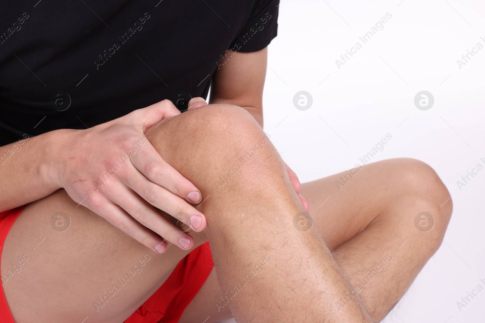 Photo of Young man suffering from pain in knee on white background, closeup