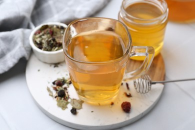 Photo of Delicious herbal tea with honey and dry leaves on white tiled table, closeup