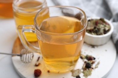 Photo of Delicious herbal tea with honey and dry leaves on white table, closeup