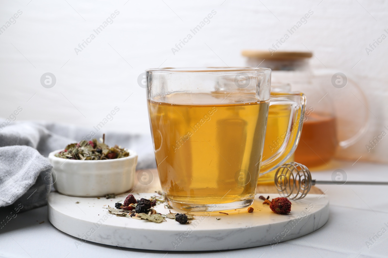 Photo of Delicious herbal tea with honey and dry leaves on white tiled table, closeup