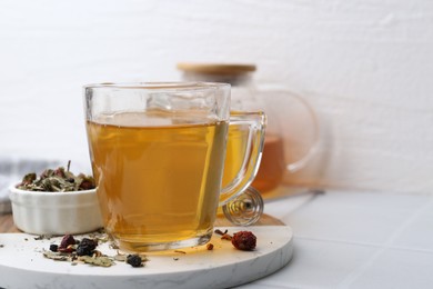 Photo of Delicious herbal tea with honey and dry leaves on white tiled table, closeup