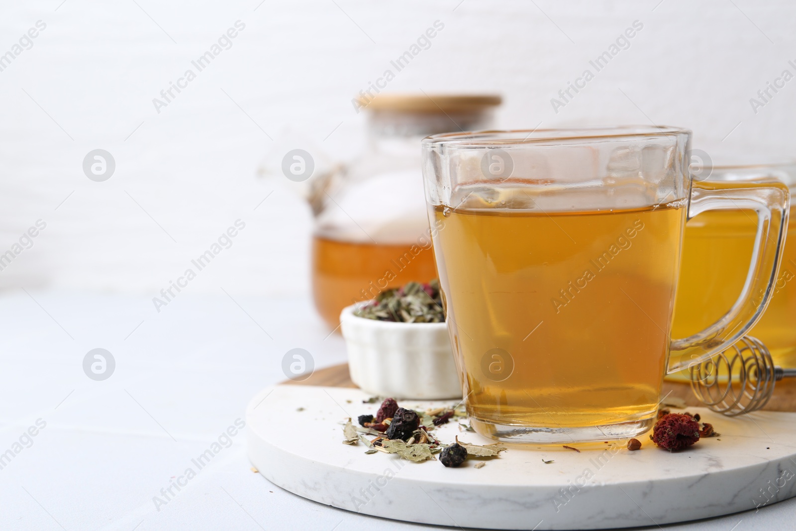 Photo of Delicious herbal tea with honey and dry leaves on white table, closeup. Space for text