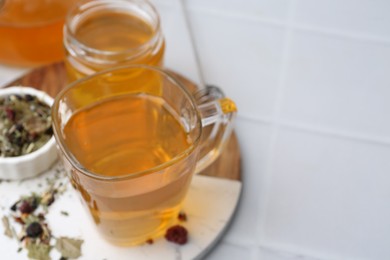 Photo of Delicious herbal tea with honey and dry leaves on white tiled table, closeup. Space for text