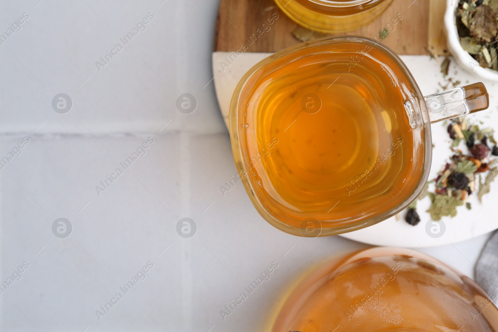 Photo of Delicious herbal tea and dry leaves on white tiled table, flat lay. Space for text